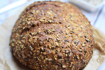 Macro, multigrain bread, on kraft paper bag on a light colored rustic table.