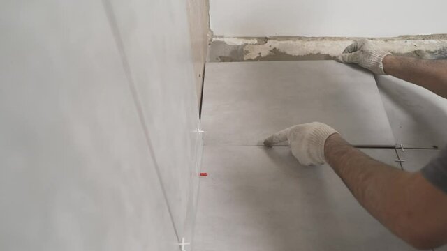 The master tiler glues the gray ceramic wall tiles. The craftsman glues the tiles to the bathroom wall.