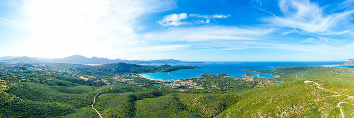 View from above, stunning aerial view of a mountain range covered by a green vegetation with a beautiful beach in the distance bathed by the mediterranean sea. Porto Rotondo, Sardinia, Italy.