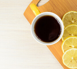 Cup of tea and slices of lemon on a wooden kitchen board, top view. Treating colds with lemon tea.