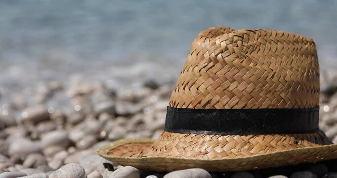 Travel concept with straw hat on pebbles beach with sea water background