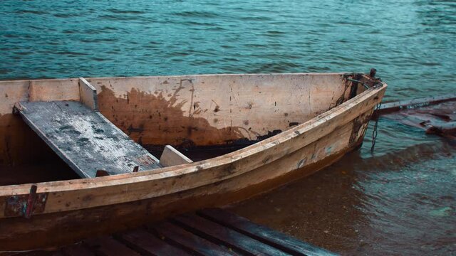 An old makeshift boat made of wood bobs on the waves. It slams its starboard side against the wooden scaffolding. The boat has two seats for passengers. The video is slow-motion.