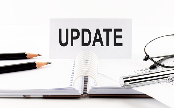 Text UPDATE on paper card,pen, pencils,glasses,financial documentation on table - business concept