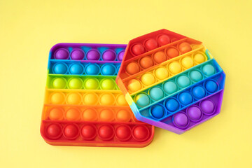 Colorful anti-stress fidget push pop it sensory toys for children isolated on yellow background. Simple dimple. Top view, flat lay. Selective focus.