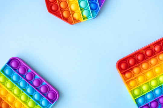 Colorful anti-stress fidget push pop it sensory toys for children isolated on blue background with copy space. Simple dimple. Top view, flat lay. Selective focus.