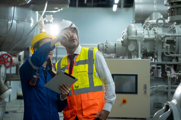 Engineer with technician working with tablet in electrical room of large industry factory.