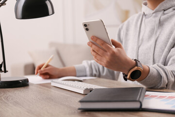 Fototapeta premium Young woman with smart watch and phone at table in office, closeup