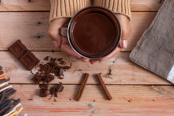 Cup of hot chocolate in woman's hands and pieces of chocolat on wooden rustic table