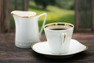  Filiżanka z poranną czarną kawą na spodku, z dzbankiem na mleko w tle