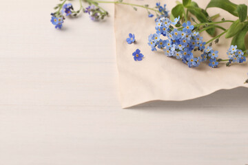 Beautiful Forget-me-not flowers and parchment on white wooden table. Space for text