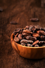 Unpeeled organic cocoa bean in bowl on wooden rustic table background. Copy space