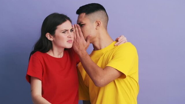The unpleasantly surprised couple pointing to the camera and whispering something in each other's ear while standing in the studio