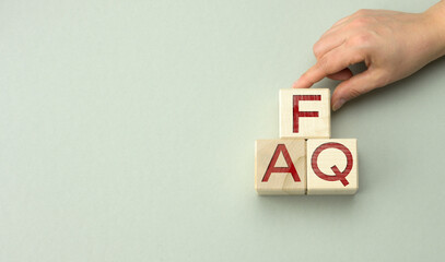 inscription FAQ (frequently asked questions) on wooden blocks on a gray background. QA concept,...