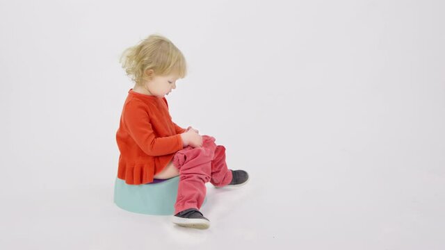 Adorable cranky tired sleepy toddler girl sitting on potty telling her parents to bring toys isolated on white studio. Infantile caprices, tantrums concept. Getting your baby accustomed to potty