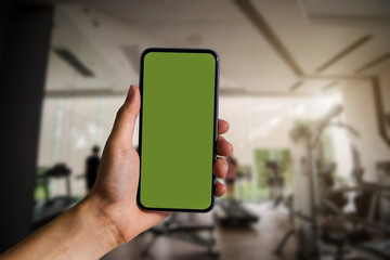 Hand held black smartphone With a blank green screen in the Gym in the morning light.