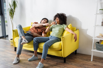 man reaching glass of water while african american woman drinking in living room