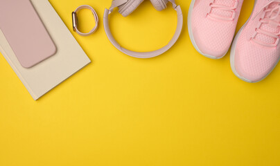 pair of pink sneakers, wireless headphones, a smartphone and a smart watch on a yellow background