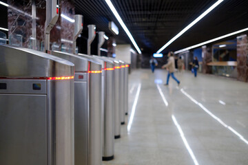 Selective focus on turnstiles at a subway station. Passengers on a blurred background.