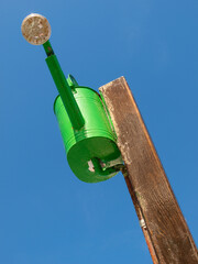 Regadera de metal verde colgada de un poste de madera a modo de ducha