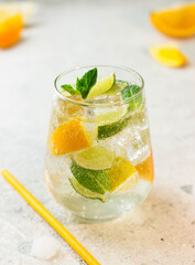 Lemonade with lemon, lime, tangerine, mint and ice cubes in glass on gray stone background. Cold summer refreshing drink or beverage.
