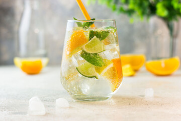 Lemonade with lemon, lime, tangerine, mint and ice cubes in glass on gray stone background. Cold summer refreshing drink or beverage.