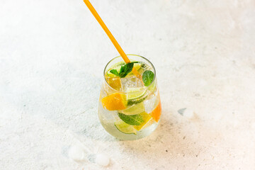 Lemonade with lemon, lime, tangerine, mint and ice cubes in glass on gray stone background. Cold summer refreshing drink or beverage.