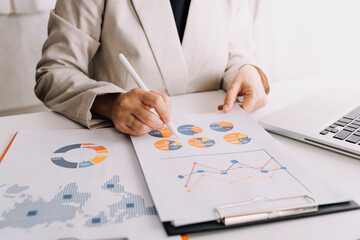 Attractive business woman working in office sitting at desk analyzing statistics holding documents...