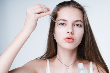 Portrait of a beautiful young girl caring for the skin applying serum with a pipette. Isolated on light background
