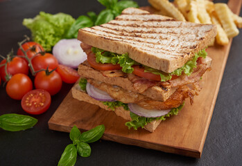 Club-sandwich with french fries. Sandwich with bacon, fried egg. Grilled and pressed toast with bacon, fried egg, tomato and lettuce served on wooden cutting board.