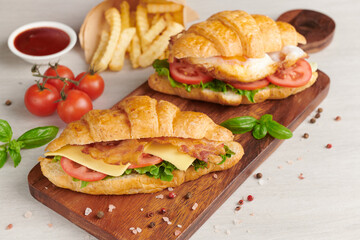two croissant sandwiches on wooden table, top view, Sandwich with bacon, fried egg. Ham, cheese, bacon, fried egg, tomato, french fries and lettuce served on wooden cutting board.