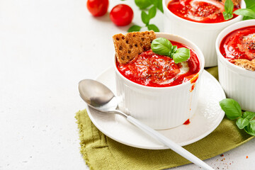 Tomato soup with crispbread and basil in white bowls on a gray background. Tasty summer food.