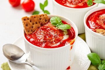 Tomato soup with crispbread and basil in white bowls on a gray background. Tasty summer food.