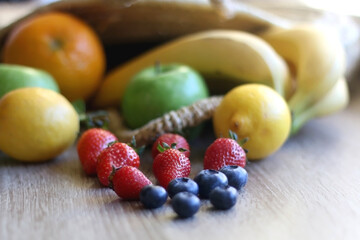 Straw bag full of various colorful fruit on wooden background. Selective focus.