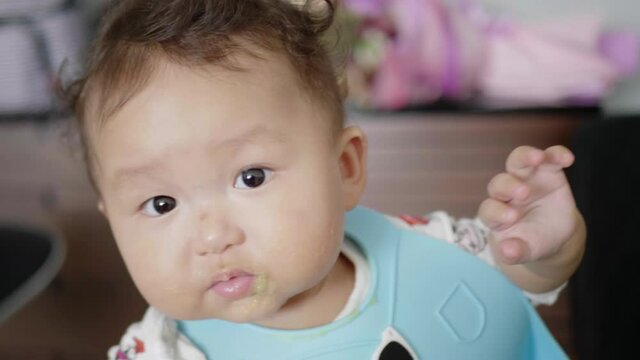 Asian baby girl happily eating solid foods.