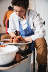 Young concentrated brunette woman shaping clay dish