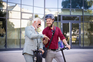 Fototapeta premium Two business men riding electric scooter in the city. Business men handshaking.