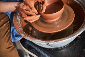 Professional ceramist shaping clay pot on special wheel