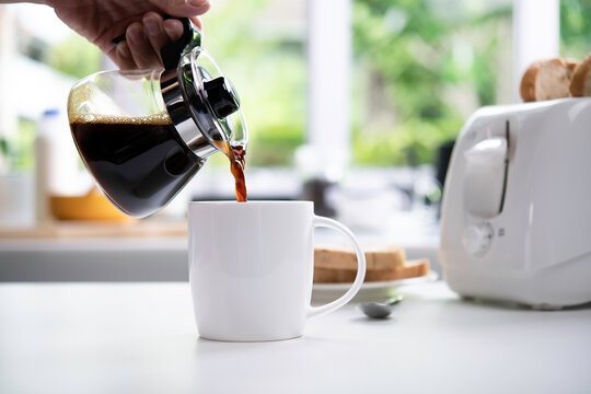 A hand pouring steaming coffee in to a cup on table in the kitchen