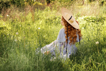 Girl in hat sits back in the garden in summer