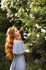Girl with hair and makeup in lilac dress at the flowering tree in summer in the garden