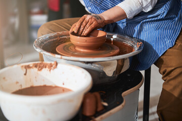 Fototapeta na wymiar Young master creating clay utensil on spinning wheel