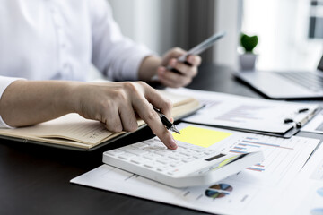 A woman pressing a white calculator and holding money, she is keeping a personal account by recording income and expenses in a notebook, personal bookkeeping to plan and manage money spending.
