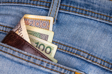 Wallet and lots of Polish banknotes sticking out of the back pocket of denim pants. Photo taken under artificial, soft light
