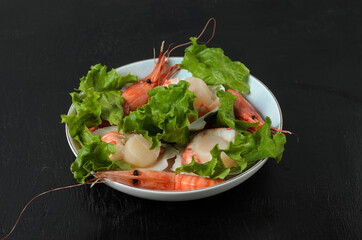 Natural raw scallop with boiled shrimp in the sink in a ceramic bowl with lettuce leaves on a dark...
