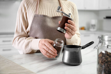 Fototapeta na wymiar Woman opening coffee grinder at table indoors, closeup