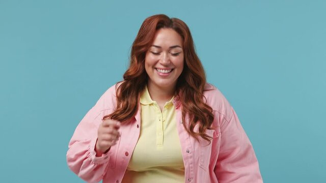 Excited cheerful fun young redhead chubby overweight woman 20s years old in pink jacket yellow tshirt laugh watch comedy movie point index finger on you isolated on pastel blue color background studio