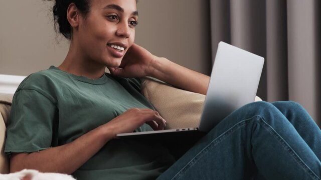 A cropped view of a positive african american woman is using her laptop computer while sitting on the sofa and petting her dog at home