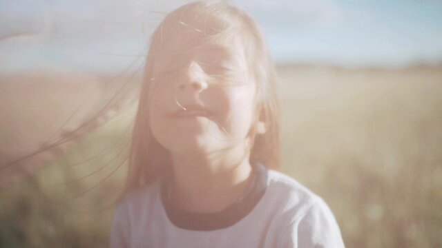 A girl stands under a transparent cloth Curtains flutter in the wind A child enjoys nature Blue sky Rays of the sun A field in dandelions Creative freedom Family vacation Slow motion