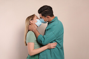 Couple in medical masks trying to kiss on beige background