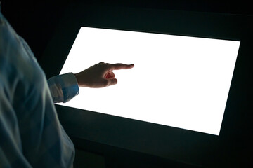 Woman hand using white blank interactive touchscreen display of electronic multimedia kiosk in dark...
